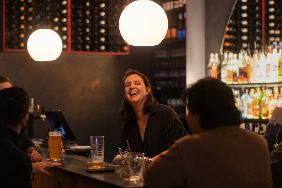 the co-owner alli laughing behind bar with regulars at We Three Bar in marrickville sydney